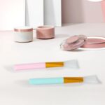 A pink and a blue silicone face mask applicator wand, side by side, showcasing their flexible bristles and ergonomic handles.